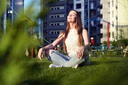 Young woman sitting in lotus position on the lawn in the courtyard of a residential block