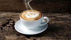 Hot cappuccino with streamed milk. Pour the hot milk made a heart. A cup of strong coffee put on the wood table with shiny dark roasted Italian coffee beans. Aroma espresso and flavor beverage.