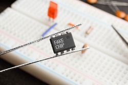 Fake chip concept: An integrated circuit held with tweezers on top of a breadboard populated with electronic components