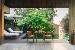 Beautiful cozy luxury breakfast for two at the private pool, Bali,Indonesia.A wooden table with an abundant healthy breakfast on the background of the pool and tropical plants.