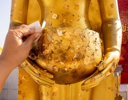 Buddhist people covered gold leaves on the Buddha statue in the temple. The gilded Buddha statue is a traditional culture of Thai Buddhists.