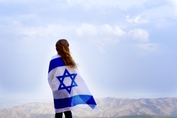 Little patriot jewish girl standing and  enjoying great view on the sky, valley and mountains with the flag of Israel wrapped around her. Memorial day-Yom Hazikaron and Yom Ha'atzmaut concept. 