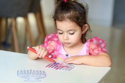 Curly brunette cute little toddler girl painting with color pen paper menorah and candle Jewish holiday Chanukah. Hebrew text : Happy Hanukkah!