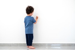 Curly cute little toddler boy painting with color pencil on the wall.