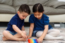 Two cute children playing with the Pop It fidget. Push pop bubble flexible fidget sensory toy provide discharge and are good for the development of kid. Soft focus.