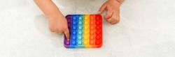 Anonymous child with colorful poppit game. Close up bunner shot of kid hands playing with colorful pop It fidget toy.