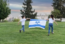 Young children running with Israeli flag. Rear view little girl and boy running with Israel flag up a hill in the sunset