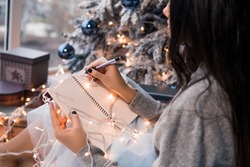 Christmas letter writing on notebook. Many garlands. Christmas , winter holidays and people concept. Letter to Santa Claus. Girl writes her wish