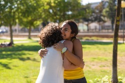 Happy close female friends greeting each other in park. Two women standing outdoors and hugging. Friendship concept
