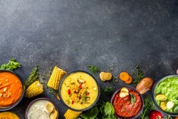 Different autumn soups set. Assortment vegetable soups in portion bowls - corn, potato, pumpkin, tomato, zucchini, broccoli cream soups. On black concrete background top view copy space