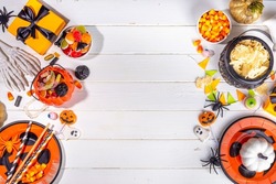 Halloween sweets and snacks table. Set of Halloween dinner party foods, candy, snacks, with holiday costume decorations, pumpkin buckets, wooden background top view copy space