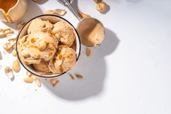 Peanut butter ice cream balls. A lot nuts gelato scoops in ceramic bowl, with caramel sauce, white kitchen background copy space
