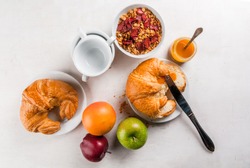 Everything you need for easy and a wholesome breakfast: croissants, jam, granola, oatmeal and dried fruit, fresh fruit (apples, oranges), a cup of tea or coffee