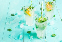 Selection of summer refreshing cocktails with mint (lemonade or mojito): with lemon, orange, lime. On light blue wooden table, bright sunlight. Copy space, close view 