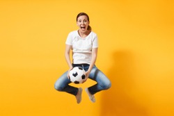 Young fun expressive European woman football fan jumping in air, cheer up support team, holding soccer ball isolated on yellow background. Sport, play football, cheer, fans people lifestyle concept