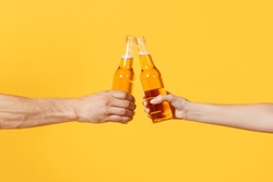 Close up cropped of woman and man two hands horizontal holding lager beer glass bottles and clinking isolated on yellow background. Sport fans cheer up. Friends leisure lifestyle concept. Copy space