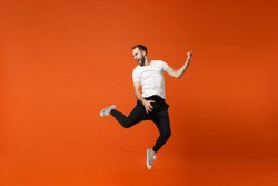 Crazy young man in casual white t-shirt posing isolated on orange wall background studio portrait. People lifestyle concept. Mock up copy space. Having fun, jumping fooling around like playing guitar