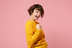 Side view of young brunette woman girl in yellow sweater posing isolated on pastel pink background studio portrait. People sincere emotions lifestyle concept. Mock up copy space. Doing winner gesture