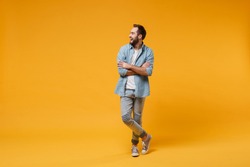 Laughing young bearded man in casual blue shirt posing isolated on yellow orange wall background, studio portrait. People lifestyle concept. Mock up copy space. Holding hands crossed, looking aside