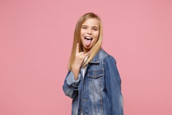 Little kid girl 12-13 years old in denim jacket isolated on pastel pink background children portrait. Childhood lifestyle concept. Mock up copy space. Showing tongue, depicting heavy metal rock sign