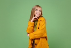 Pensive little blonde kid girl 12-13 years old in yellow coat posing isolated on pastel green background children portrait. Childhood lifestyle concept. Mock up copy space. Put hand prop up on chin
