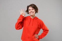 Smiling cute young brunette woman girl in casual red hoodie posing isolated on grey wall background studio portrait. People sincere emotions lifestyle concept. Mock up copy space. Showing OK gesture