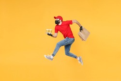 Fun jumping delivery man guy employee in red cap mask gloves hold craft paper packet food coffee isolated on yellow background studio. Service quarantine pandemic coronavirus virus 2019-ncov concept