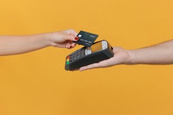 Close up cropped photo of female and male hold wireless modern bank payment terminal to process acquire credit card payments isolated on yellow background. Money, achievement, career wealth concept