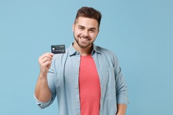 Smiling young bearded guy 20s in casual shirt posing isolated on pastel blue wall background studio portrait. People sincere emotions lifestyle concept. Mock up copy space. Hold credit bank card