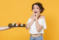 Young woman girl in casual clothes hold in hand gives takes makizushi sushi roll served on black plate traditional japanese food isolated on yellow background studio portrait People lifestyle concept