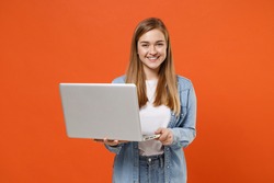 Smiling young woman girl in casual denim clothes posing isolated on orange background studio portrait. People sincere emotions lifestyle concept. Mock up copy space. Working on laptop pc computer