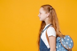 YSide profile view young redhead school teen girl 12-13 years old pony tails in white t-shirt blue denim uniform backpack isolated on yellow background children studio portrait Kids education concept.