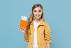 Smiling little blonde kid girl 12-13 years old in yellow jacket isolated on blue background. Passenger traveling abroad to travel on weekends getaway. Air flight journey concept. Hold passport ticket