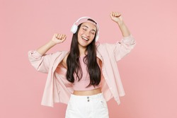 Funny young asian woman in casual clothes cap posing isolated on pastel pink background studio portrait. People lifestyle concept. Mock up copy space. Listening music with headphones, dancing
