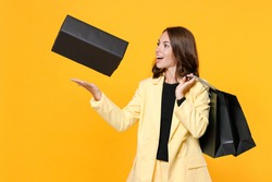 Funny young brunette woman 20s in basic light suit jacket hold package bags throwing box with purchases after shopping looking aside isolated on yellow background, studio portrait. Black friday sale
