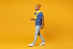 Full length side view of smiling cheerful handsome funny young african american man 20s in blue t-shirt hat walking going looking aside isolated on bright yellow colour background, studio portrait