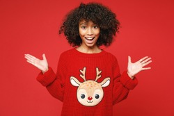 Little surpised african american curly kid girl 12-13 years old wear knitted cozy deer Christmas sweater say wow isolated on bright red background children studio portrait Childhood lifestyle concept