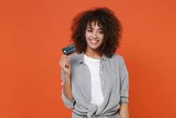 Smiling young african american woman 20s in gray casual clothes isolated on orange background studio portrait. People sincere emotions lifestyle concept. Mock up copy space. Hold credit bank card