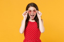 Excited young brunette woman 20s in red summer dress, eyeglasses posing isolated on yellow wall background studio portrait. People emotions lifestyle concept. Mock up copy space. Keeping mouth open