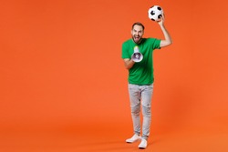 Full length portrait funny man football fan in basic green t-shirt cheer up support favorite team with soccer ball screaming in megaphone isolated on orange background. People sport leisure concept