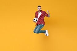 Full length portrait screaming man football fan in red shirt cheer up support favorite team with soccer ball jumping doing winner gesture isolated on yellow background. People sport leisure concept