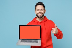 Young caucasian smiling web designer bearded man 20s in casual red orange hoodie hold laptop pc computer, blank screen workspace area show thumb up gesture isolated on blue background studio portrait