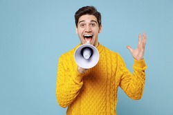 Young caucasian surprised shocked student man 20s in casual knitted yellow fashionable sweater scream aside shout hot news in megaphone spread hand isolated on blue color background studio portrait