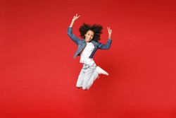 Full length of funny little african american kid girl 12-13 years old in denim jacket jumping showing victory sign isolated on red background children studio portrait. Childhood lifestyle concept