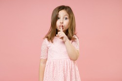 Little fun kid girl 5-6 years old wears rosy dress say secret hush be quiet with finger on lips shhh gesture isolated on pastel pink background child studio portrait. Mother's Day love family concept