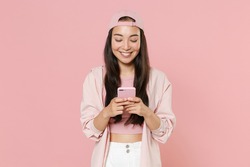 Smiling young asian woman girl in casual clothes cap posing isolated on pastel pink wall background studio. People lifestyle concept. Mock up copy space. Using mobile cell phone, typing sms message