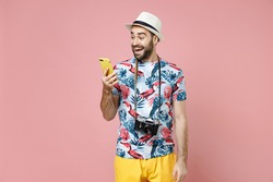 Excited young traveler tourist man in summer clothes, hat using mobile cell phone typing sms message isolated on pink background. Passenger traveling abroad on weekends. Air flight journey concept