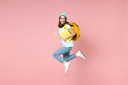 Full length side view of excited young woman student in blue t-shirt hat glasses backpack hold notebooks jump isolated on pink background studio. Education in high school university college concept