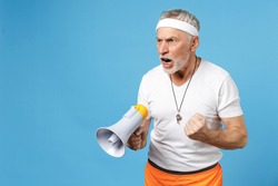 Elderly gray-haired sportsman trainer instructor angry coach man 60s in sportswear white t-shirt whistle scream shout in megaphone command clench fist isolated on blue background Fitness sport concept