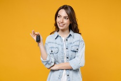 Young smiling dreamful pensive wistful happy rich brunette woman 20s wearing stylish denim shirt white t-shirt holding in hands car keys look aside isolated on yellow color background studio portrait